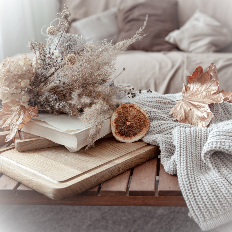 Seasonal Assistance Coffee Table with Seasonal accents and decorations on it including flowers, dried orange, leaf, and a knit blanket.